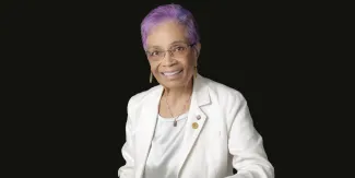 Headshot of a woman in a white suit with purple hair