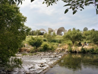 View across a river toward a concrete pavilion nestled in the landscape