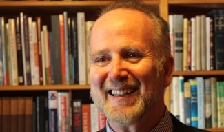 Headshot of man with beard in front of bookcase