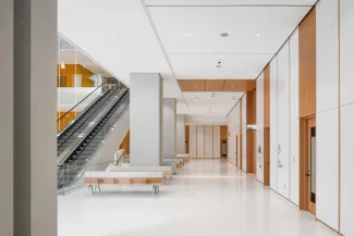 PUBLIC CORRIDOR WITH CUSTOM WOOD VENEER AND EXTRUDED ALUMINUM SEATING ON LEFT AND WHITE QUARTZ WALL PANELS IN BEECH WOOD TRIM WALLS ON RIGHT