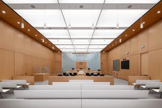 CEREMONIAL COURTROOM WITH BEECH VENEER WALLS AND MILLWORK, LUMINOUS CEILING, AND WHITE SOLID SURFACE PUBLIC SEATING