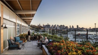 External view of residents gathering on a patio with partially covered roof and natural landscape in the background.