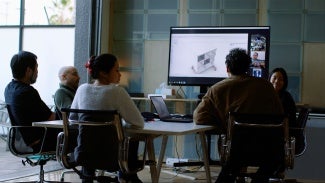 photo of people sitting around a table looking at a screen with architectural drawings.
