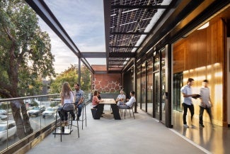 View from DPR Sacramento Zero Net Energy Office looking west on exterior terrace showing large operable window wall, solar shade trellis and view to existing trees and J street
