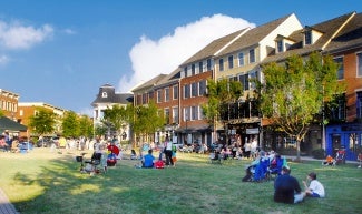 Residents sit on the community green on a sunny day; multifamily housing faces the park.