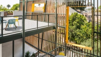 Elevated outdoor patio against a grated wall that overlooks green space. A large square frame in the middle provides an unobstructed view.