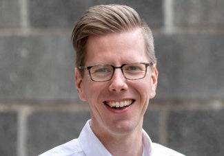 headshot of a man with short blonde hair wearing glasses and a white shirt. 