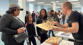 A man shows a wooden model to a woman and two children at an event.