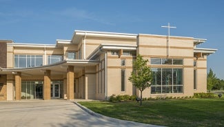 Exterior view of a light brick church at day. 