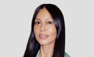 Woman with long dark hair standing in front of a light background.