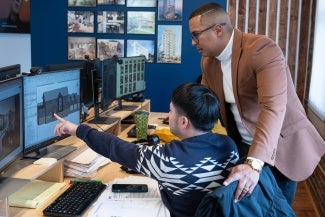 A man showing another man rendering of a house on his computer.