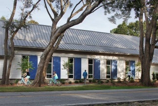 Building exterior with white cladding and blue shutters. There are three large trees in the foreground