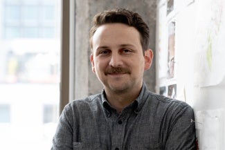 Headshot of a man with dark hair and a mustache wearing a gray shirt. 