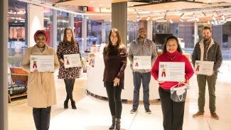 Six individuals stand in a lobby area holding award certificates.