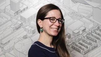 Headshot of a woman with long hair wearing glasses. She is standing in front of a site plan. 