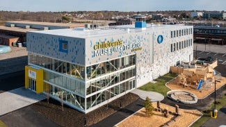 Arial shot of a children's museum at daytime. There is a wooden play structure in the foreground. 