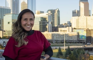 a woman with long hair and a red shirt stands in front of a cityscape.