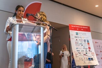 Two women stand behind a transparent lectern at a conference.