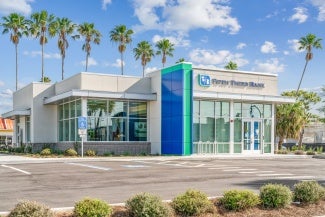 External view of a one story bank in a parking lot with palm trees in the background.