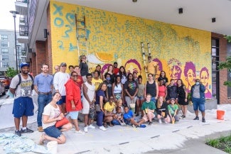 A group of people in front of an external wall mural they have been working on. 