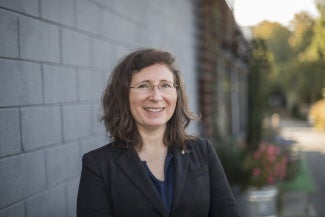 Headshot of a woman with wavy dark hair wearing a dark jacket and glasses