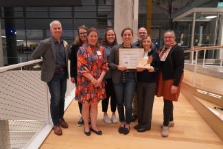A group of people posed for a photo in an atrium. The person at the center of the group is holding a certificate. 
