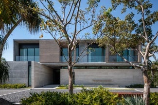 Exterior view of a gray building at day. There are trees in the foreground. 