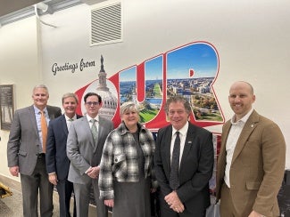 people standing in front of a sign that says "Greetings from TOUR" (capitol tour sign)