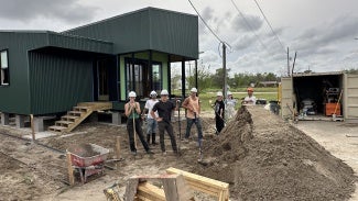 seven students wearing hard hats pose at construction site 