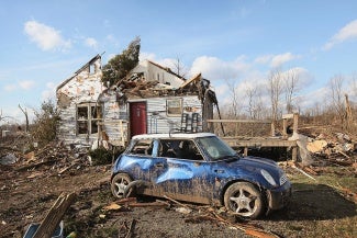 tornado-damaged house and blue mini cooper sitting in a field 