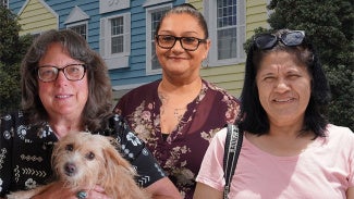 three women one holding a dog against a house background
