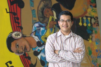 hispanic latinx man posing in front of a mural depicting musical notes and people playing instruments