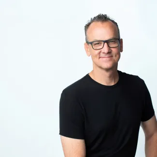 Headshot of a man in a black shirt and glasses