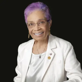 Headshot of a woman in a white suit with purple hair