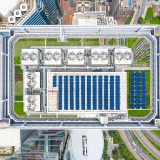 A bird's eye view of the top of a building in a city, outfitted with solar panels and greenery
