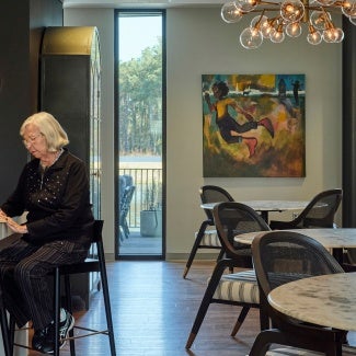 Resident sits at high-top table with lower tables and chairs behind her. 