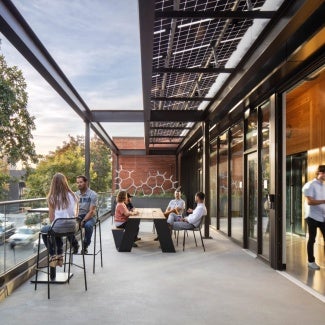 View from DPR Sacramento Zero Net Energy Office looking west on exterior terrace showing large operable window wall, solar shade trellis and view to existing trees and J street