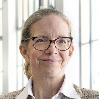 headshot of Elizabeth Plater-Zyberk; woman standing in front of windows wearing glasses with her hair pulled back