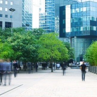 people walking around the exterior of buildings with green space