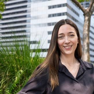 Headshot of a woman with long dark hair in a dark blouse standing outside 