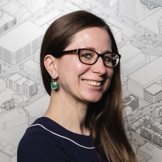 Headshot of a woman with long hair wearing glasses. She is standing in front of a site plan. 