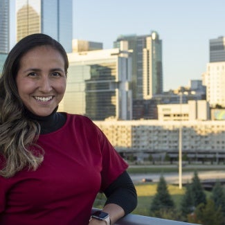 a woman with long hair and a red shirt stands in front of a cityscape.