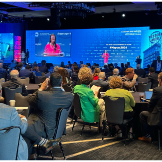 Lakisha Woods speaks at a podium and can be seen on large screen in a ballroom