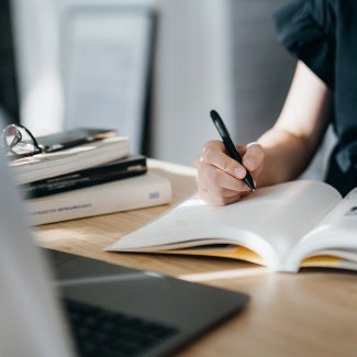 Cropped shot of focused young Asian woman reading book and making notes at home, concentrates on her studies. Further education, continuous learning concept - stock photo