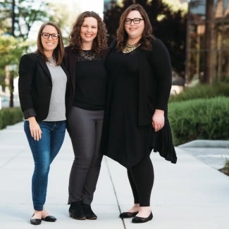 This is an image of three women architects standing and posing together for a picture on a sidewalk outside