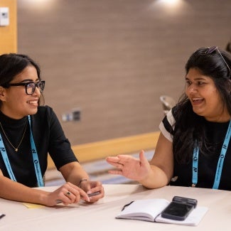 two women talking while sitting next to each other at a table