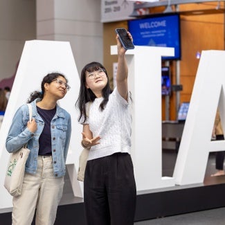 Two women taking a selfie in front of AIA logo