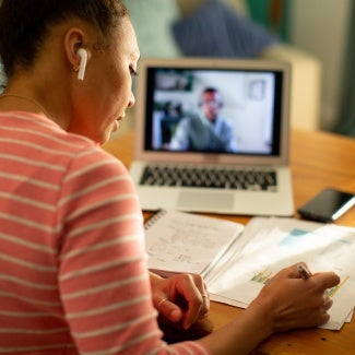 Woman taking notes as she watches a class on her laptop computer
