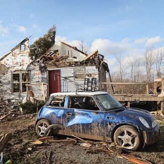 tornado-damaged house and blue mini cooper sitting in a field 
