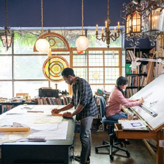 Two people stand back to back, each working at their own large surface in the work area/office